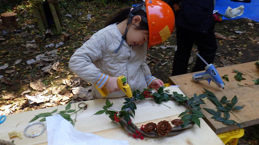 グルーガンを使い、木の実や葉でクリスマスリースを手作りする子供